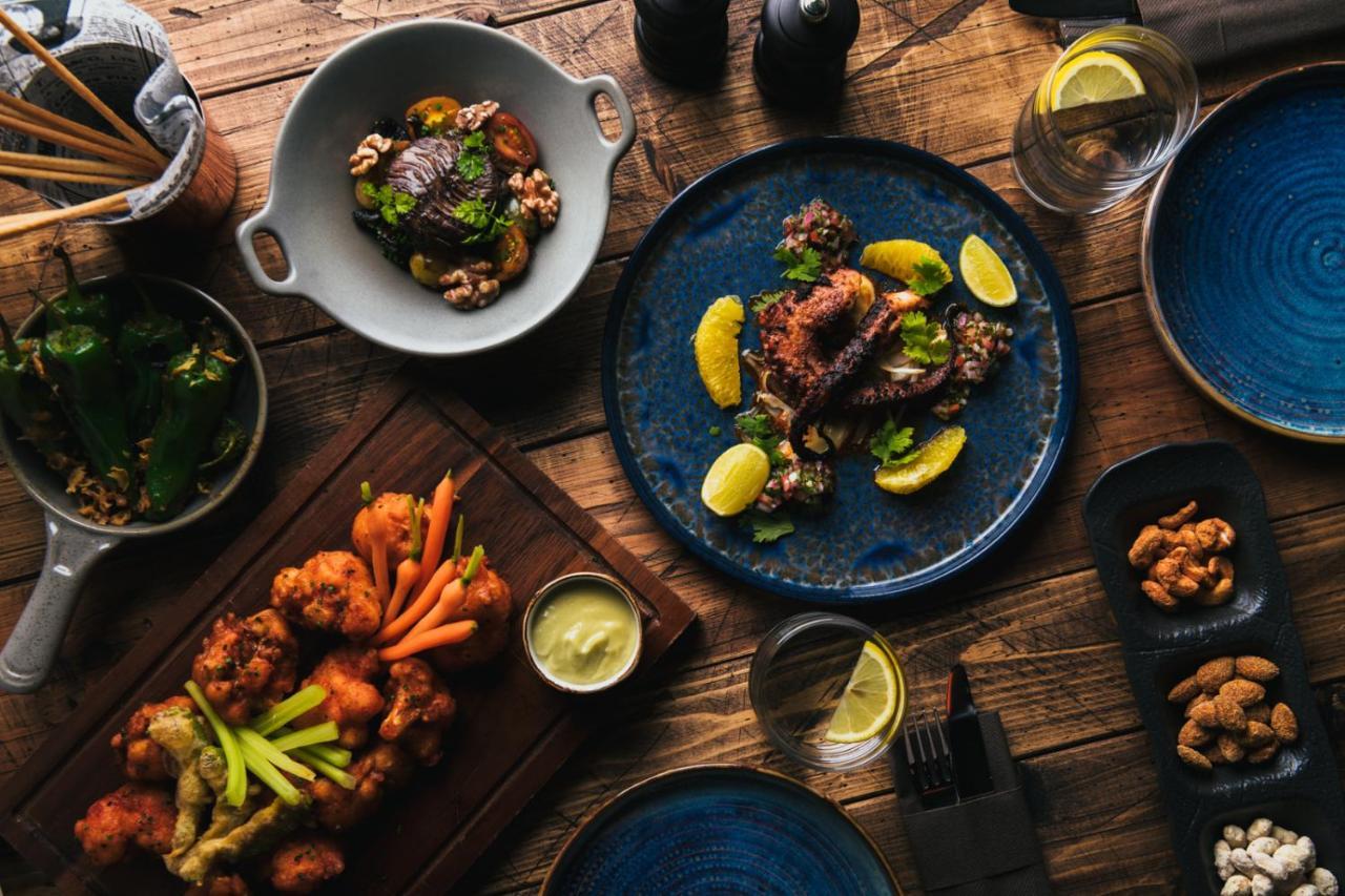 Five Jumeirah Village Dubai Esterno foto The photo displays a beautifully arranged spread of various dishes on a wooden table. 

1. In the center, there's a blue plate featuring a main dish garnished with lemon slices and fresh herbs.
2. To the left, another dish includes fried pieces, like