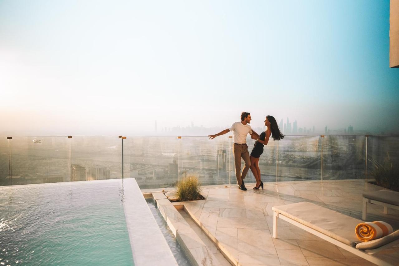 Five Jumeirah Village Dubai Esterno foto The image shows a couple dancing together on a terrace or balcony with a view of a city skyline in the background. They appear to be enjoying a romantic moment, surrounded by a luxurious setting that includes a swimming pool. The atmosphere is bright