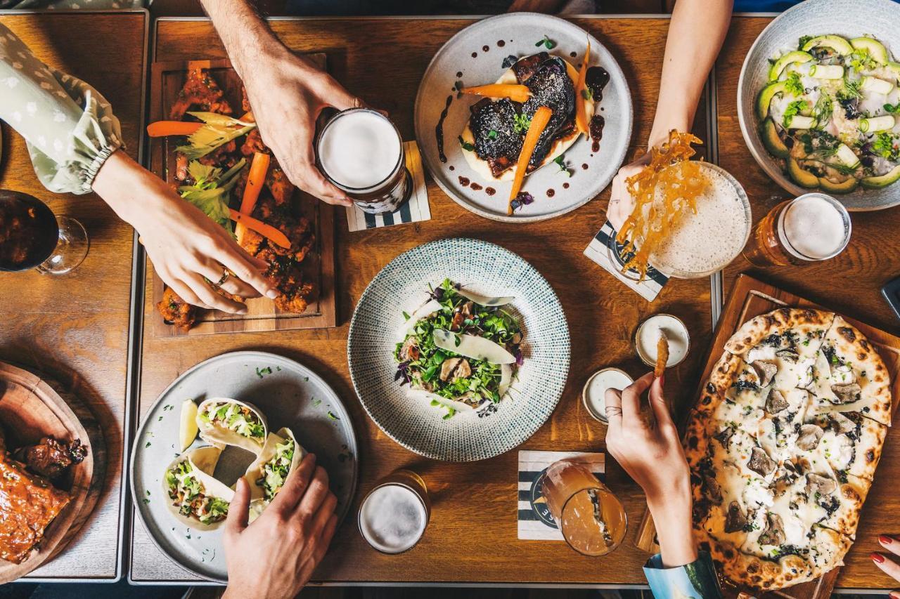 Five Jumeirah Village Dubai Esterno foto The photo displays a table filled with a variety of delicious food and drinks. There are several dishes, including a colorful salad in a round bowl, tacos, and what appears to be a pizza. On the side, there are also wooden platters with grilled veget