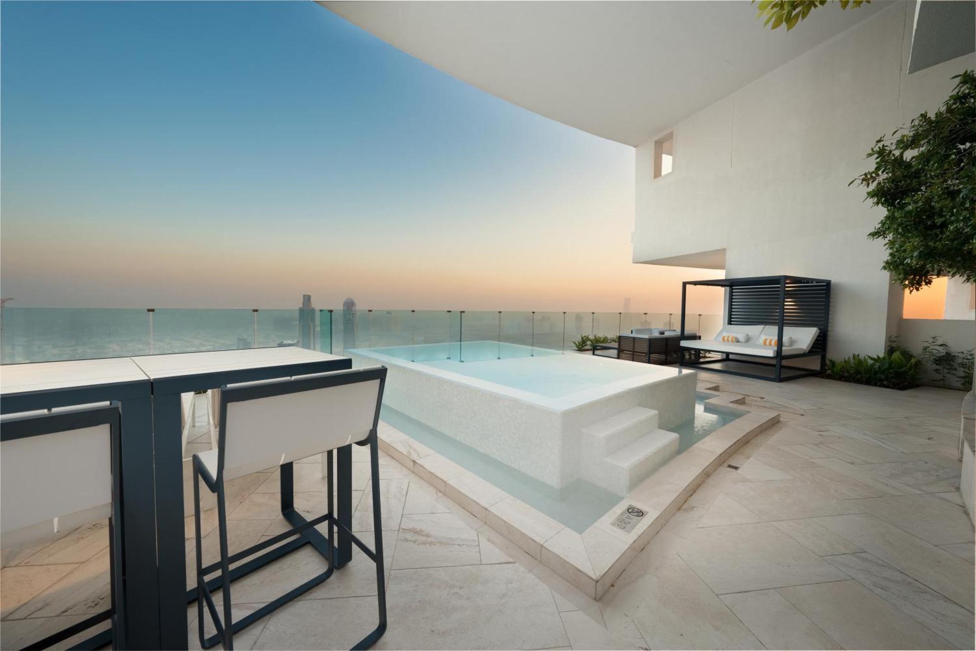 Five Jumeirah Village Dubai Esterno foto The photo depicts a luxurious outdoor space featuring a small infinity pool or hot tub that overlooks a scenic view. There is a stylish seating area nearby with modern furniture, including a table and chairs. The surroundings have a minimalist design