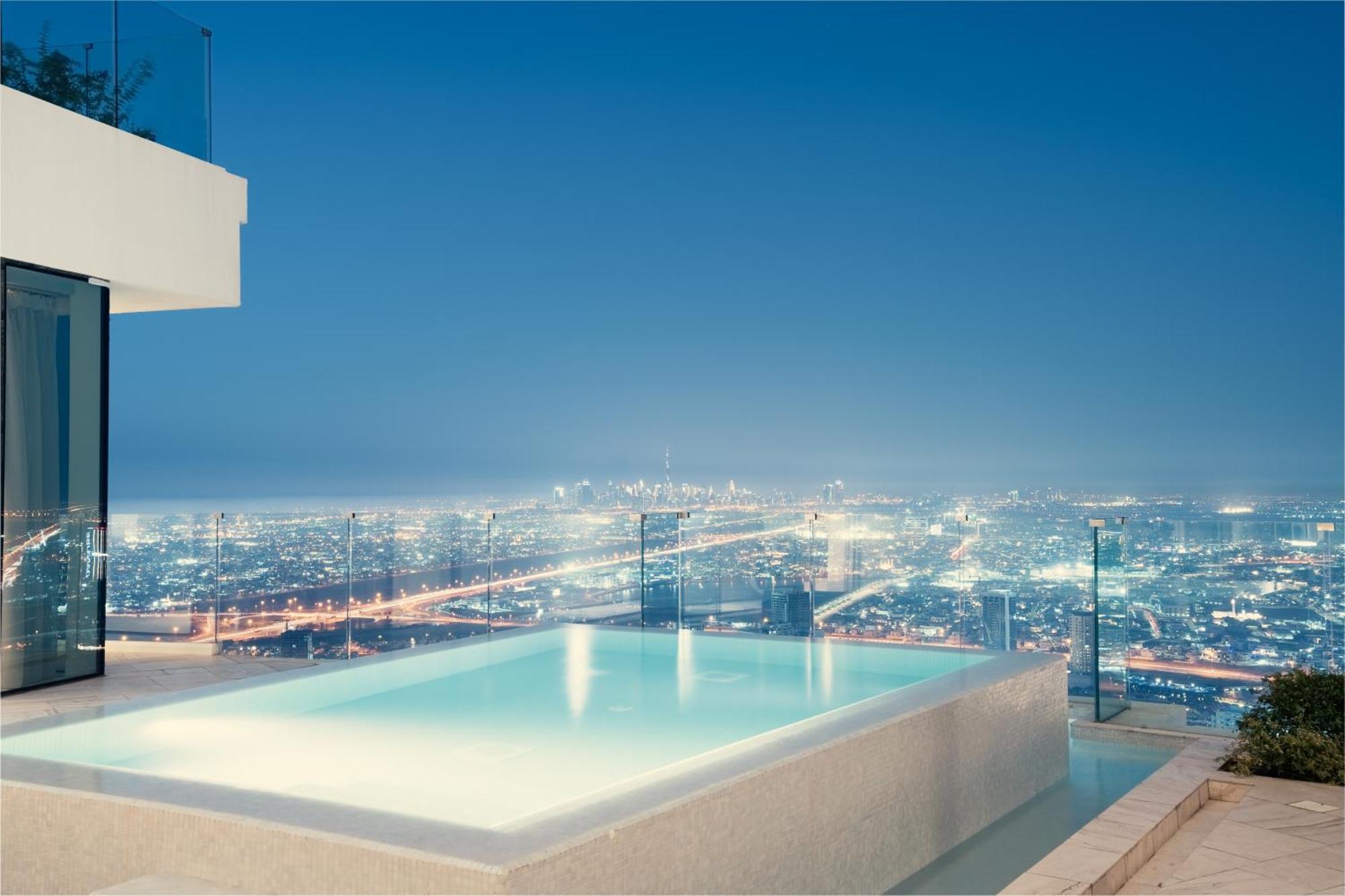 Five Jumeirah Village Dubai Esterno foto The photo showcases a luxurious infinity pool situated on an elevated terrace, overlooking a sprawling cityscape at night. The pool's water has a serene glow, reflecting the city lights below, which shimmer and create a vibrant backdrop. The architec
