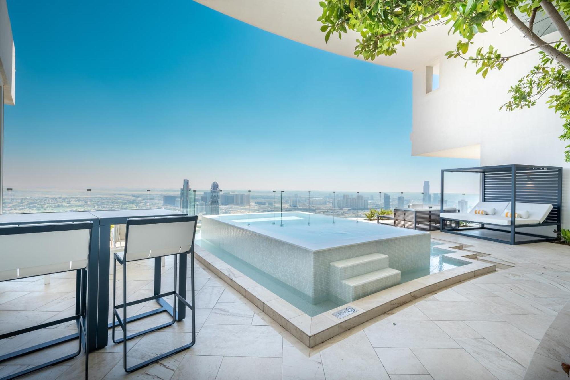 Five Jumeirah Village Dubai Esterno foto The photo shows a modern outdoor space featuring a sleek infinity pool. The pool appears to be situated on a terrace with a stunning view of a city skyline or landscape in the background. There are elegant lounge chairs and a shaded cabana area, crea