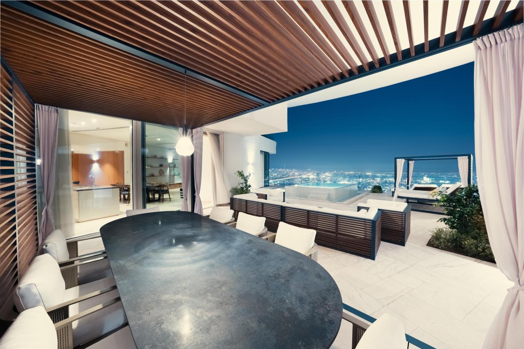 Five Jumeirah Village Dubai Esterno foto The photo shows a modern outdoor dining area with a sleek, curved table surrounded by several chairs. It features a stylish wooden ceiling with slats, creating a shaded atmosphere. In the background, large glass doors lead to the interior of a house,