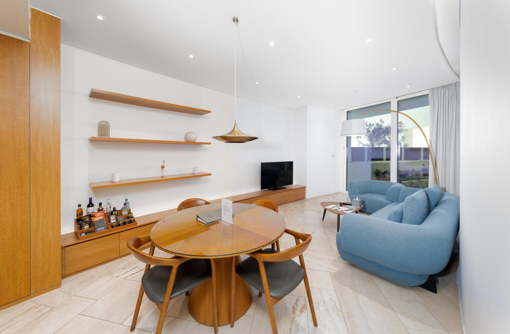 Five Jumeirah Village Dubai Esterno foto The image shows a modern living space that features a cozy and stylish design. On one side, there is a round wooden dining table surrounded by four chairs. The table is set with a small item, possibly a decorative piece or a book. 

A pendant light h