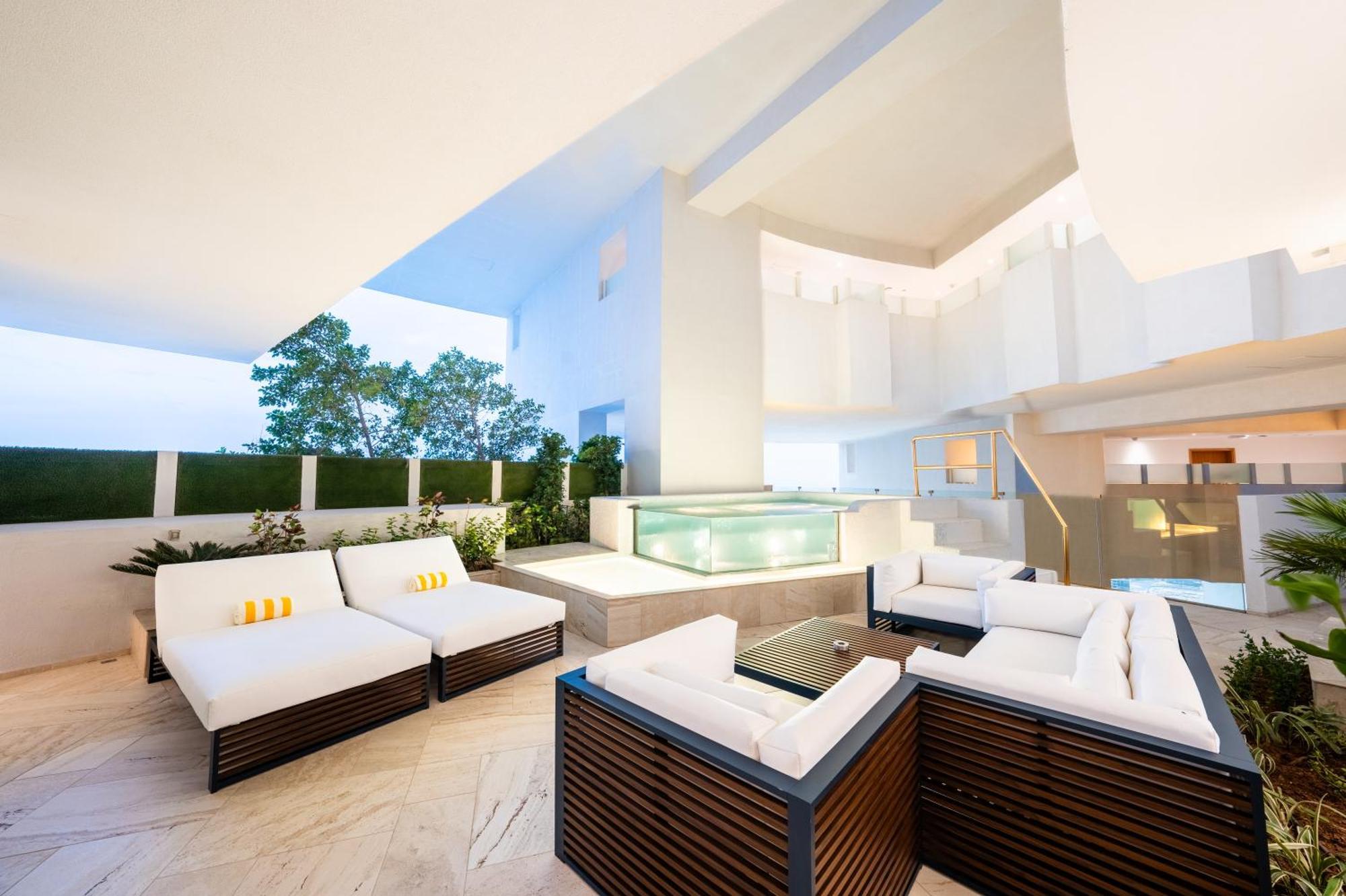 Five Jumeirah Village Dubai Esterno foto The photo depicts a modern outdoor lounge area featuring comfortable seating arrangements. There are several white sofas with dark wooden frames, arranged around a glass coffee table. In the background, there is a sleek water feature or pool, surroun