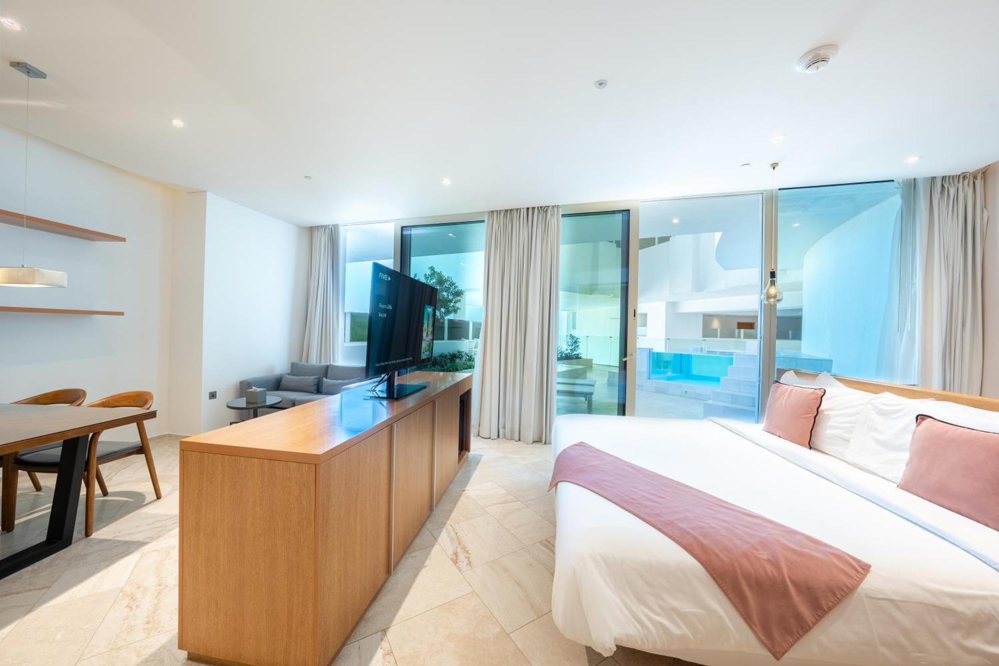 Five Jumeirah Village Dubai Esterno foto The photo shows a modern hotel room or a studio apartment. It features a large window with sheer curtains, allowing natural light to fill the space. There’s a double bed with a white bedspread and a light pink throw blanket at the foot. Opposite the 