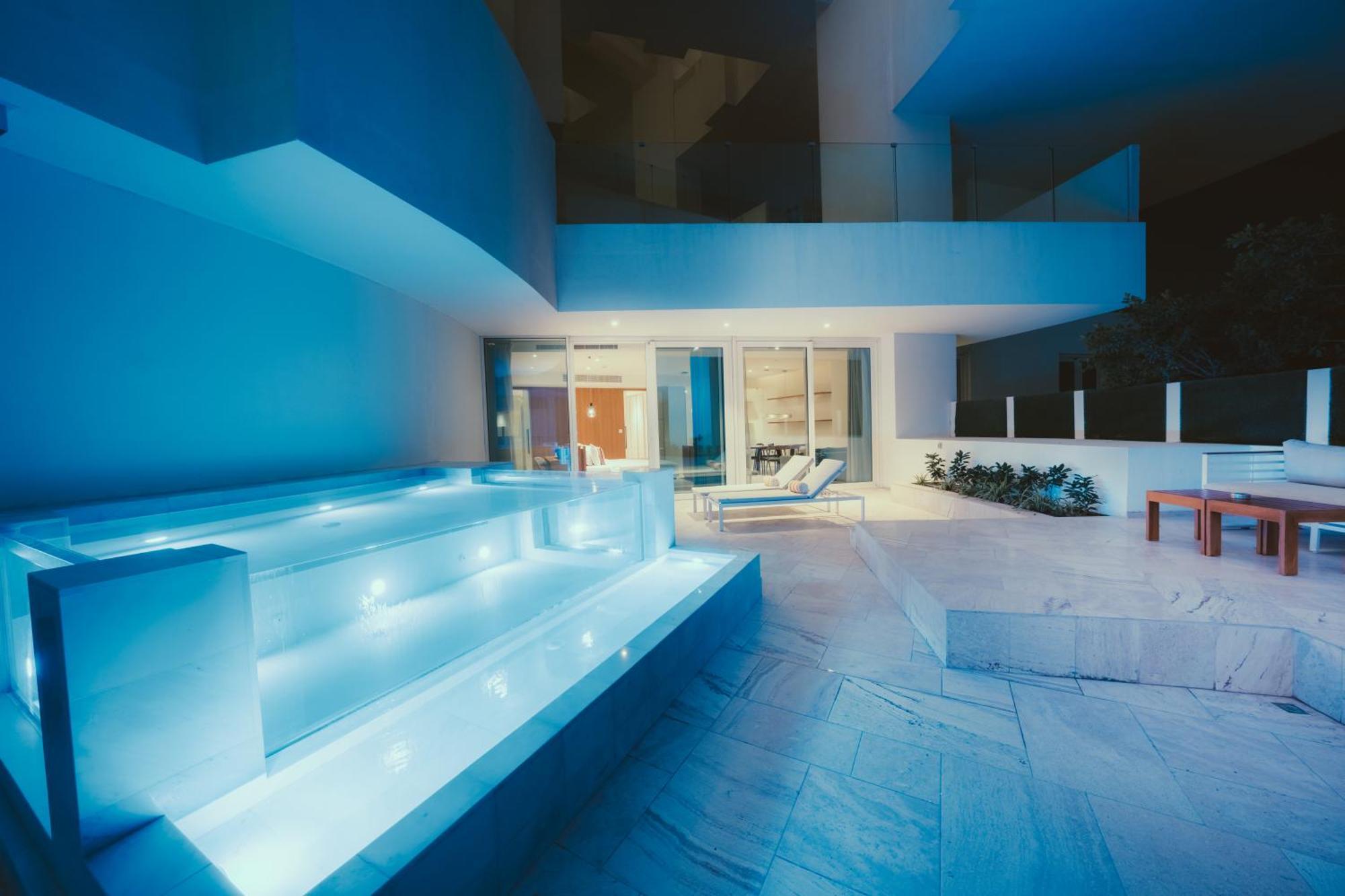 Five Jumeirah Village Dubai Esterno foto The photo shows a modern outdoor area, likely part of a contemporary home. It features a stylish, illuminated staircase leading down to a pool or water feature, with soft blue lighting that creates a serene atmosphere. In the background, large glass 