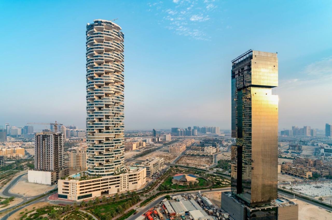 Five Jumeirah Village Dubai Esterno foto The photo shows two distinctive skyscrapers located in an urban area. On the left, there is a tall, cylindrical building with a unique, modern design characterized by its twisting, spiral shape and balconies at various levels. To the right, there is 