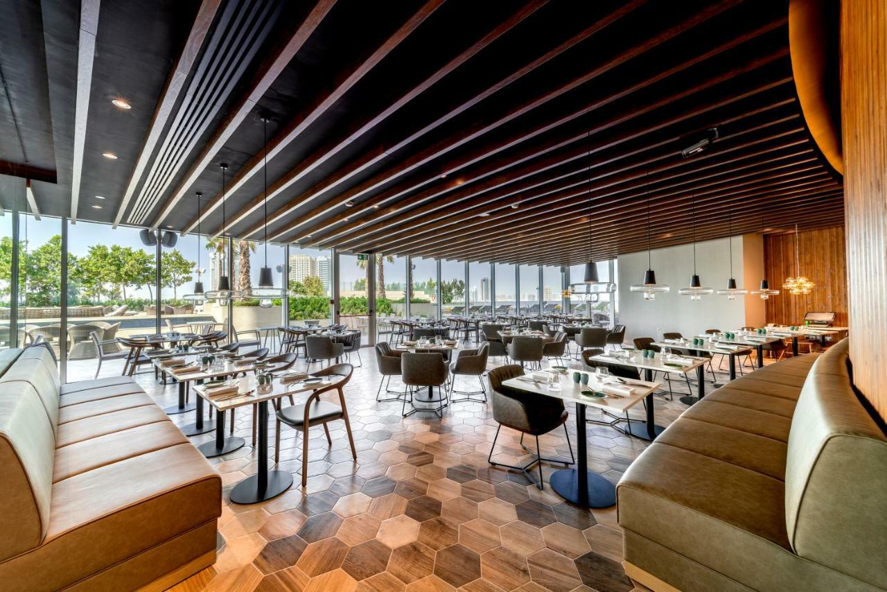Five Jumeirah Village Dubai Esterno foto The photo shows the interior of a modern restaurant. It features a spacious layout with a combination of wooden and tiled flooring, characterized by hexagonal tiles. The ceiling has a modern design with wooden beams that add a sophisticated touch. Th